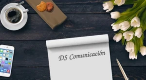 imagen de una mesa con una libreta con DS comunicación escrito, una taza de café y cookies