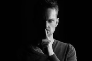 imagen oscura en blanco y negro de una persona pidiendo silencio para mentener la privacidad
