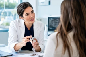 Profesional sanitaria explicando un tratamiento a una paciente en una consulta clínica.